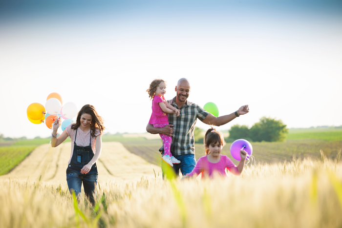 family walking through field holding balloons